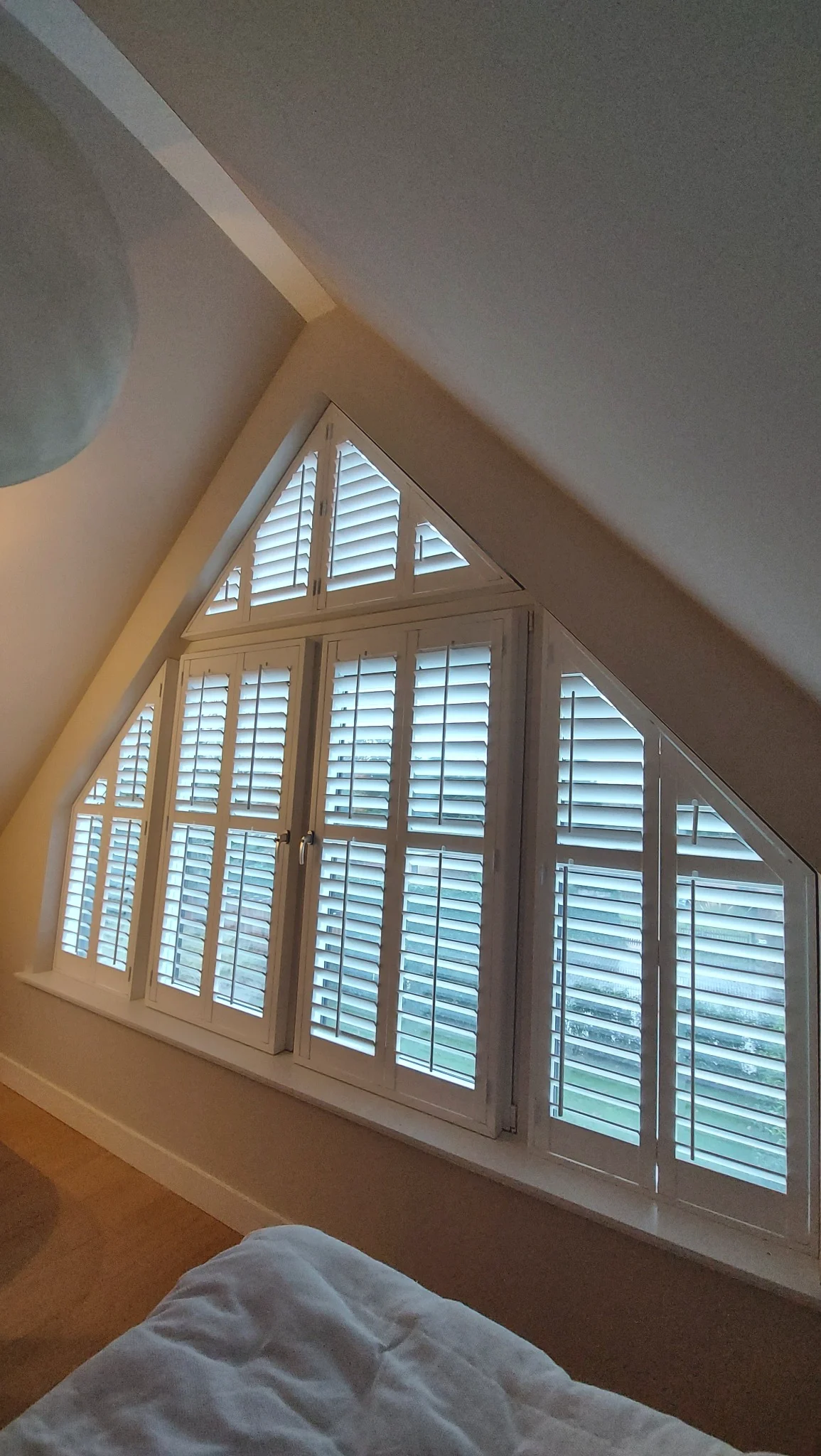 Witte shutters in een puntvormig slaapkamerraam in Huizen